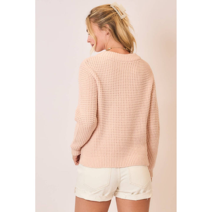 Woman wearing a light pink sweater and white shorts against a plain background