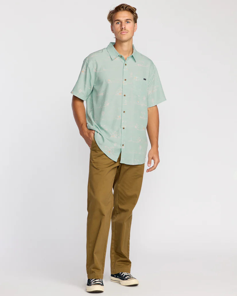 Man wearing a light green short-sleeve shirt and brown pants on a white background